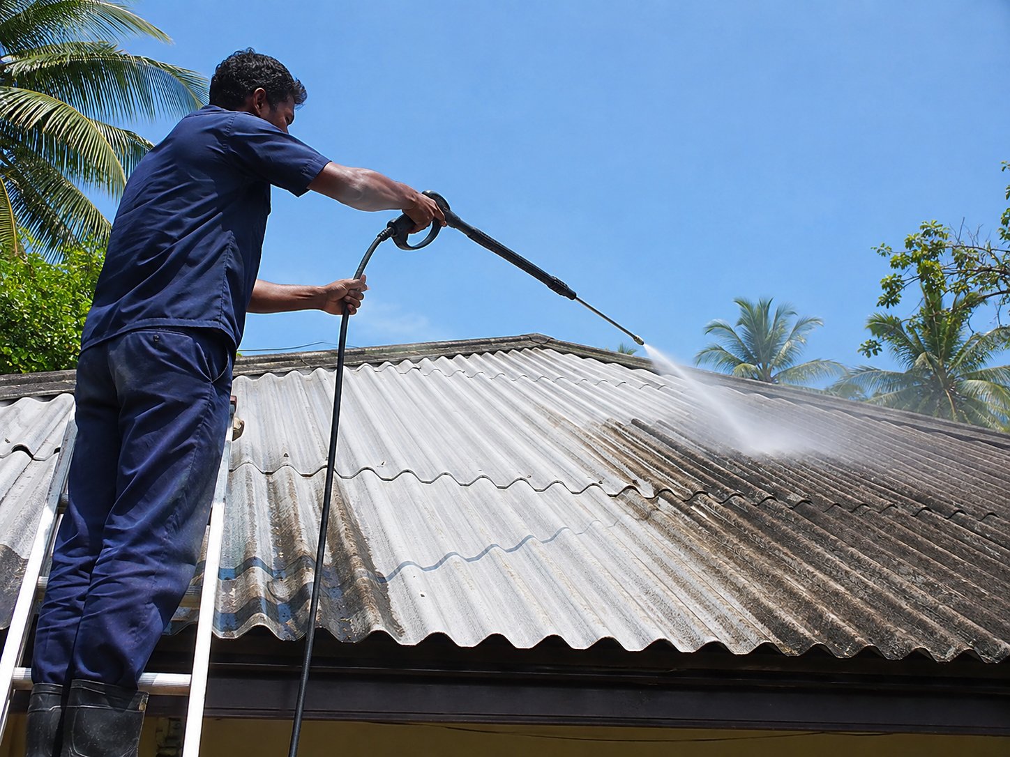 Roof pressure washing in progress, water spraying across tiled roof
